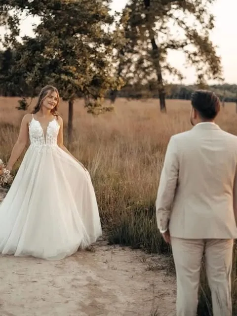 Eine Braut im weißen Kleid dreht sich auf einem Sandweg zu ihrem Bräutigam um.