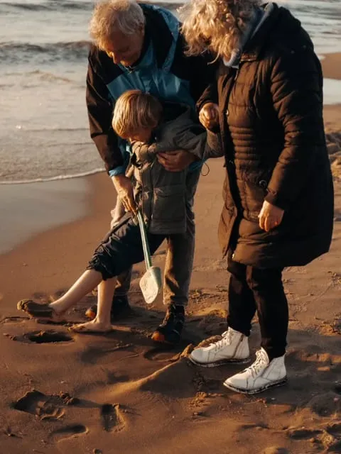 Eine Familie beugt sich am Strand über etwas im Sand.