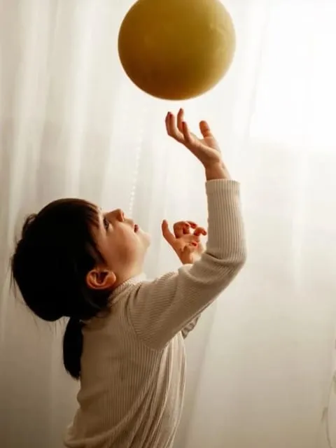 Ein kleines Mädchen streckt die Arme nach einem Luftballon aus.
