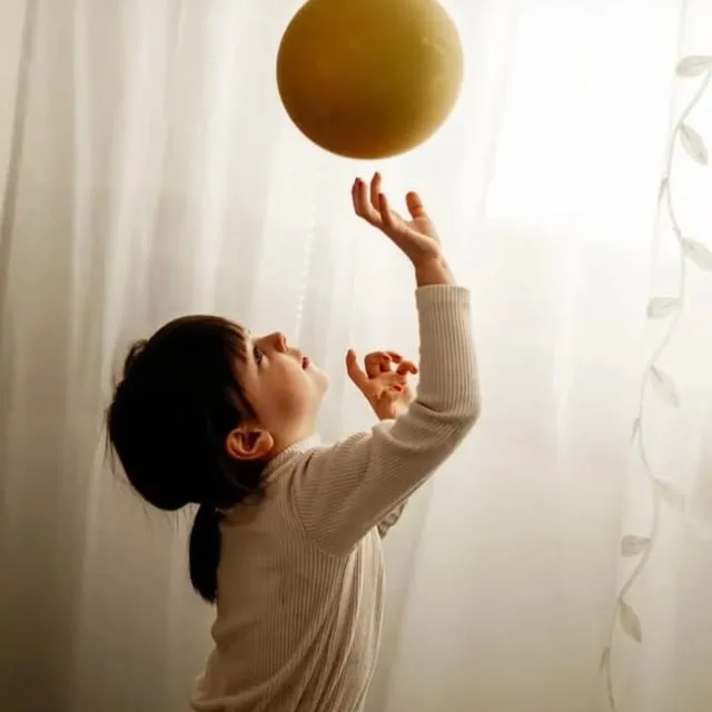 Ein kleines Mädchen streckt die Arme nach einem Luftballon aus.