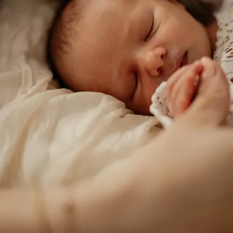 Ein schlafendes Neugeborenes liegt eingewickelt in einer hellen Decke.